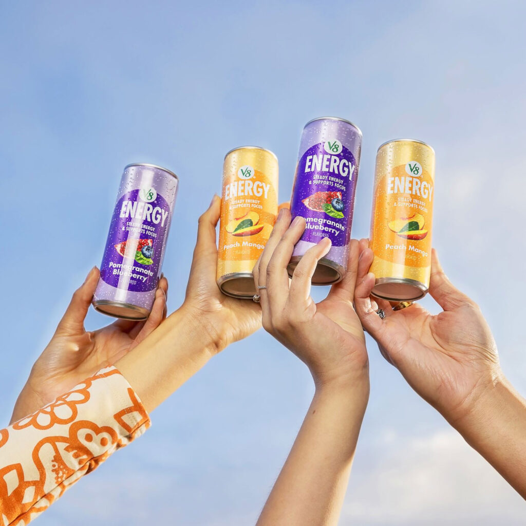 Hands holding purple and orange energy drink cans.